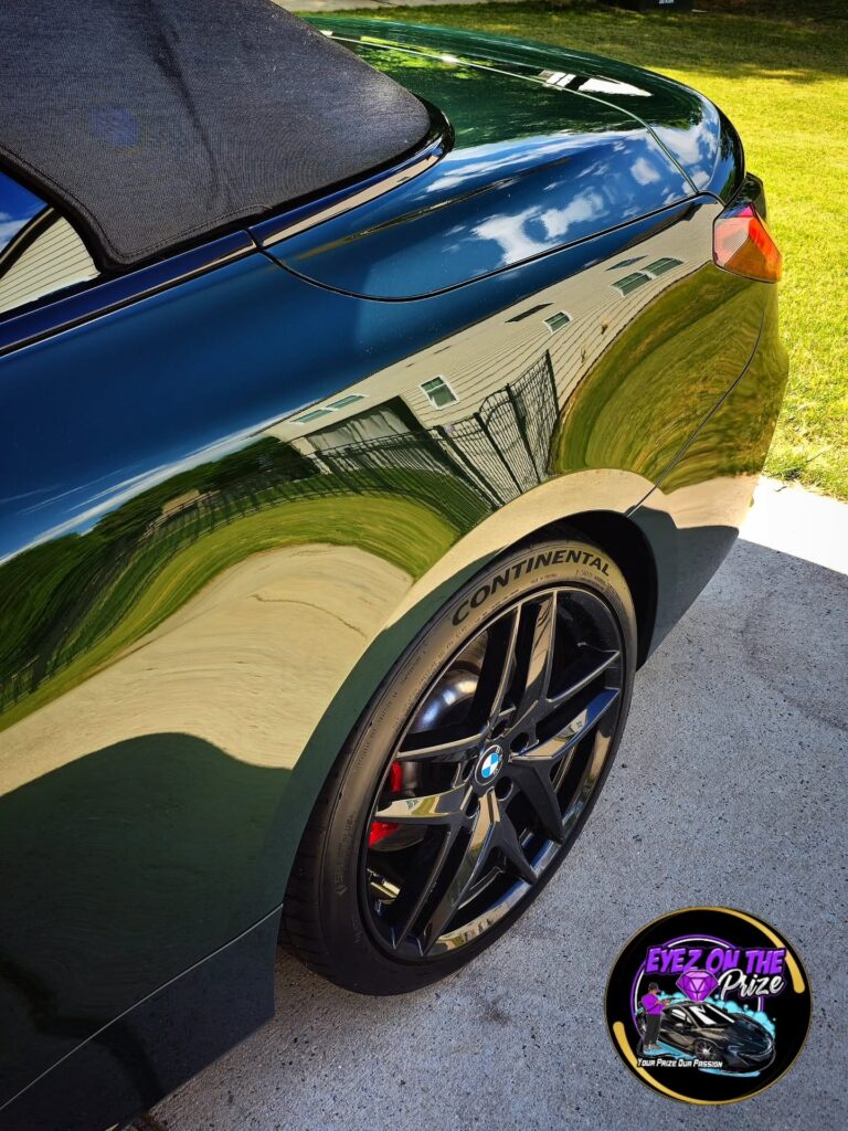 Rear quarter panel of a dark green BMW convertible with glossy reflective paint and black double-spoke wheel with Continental