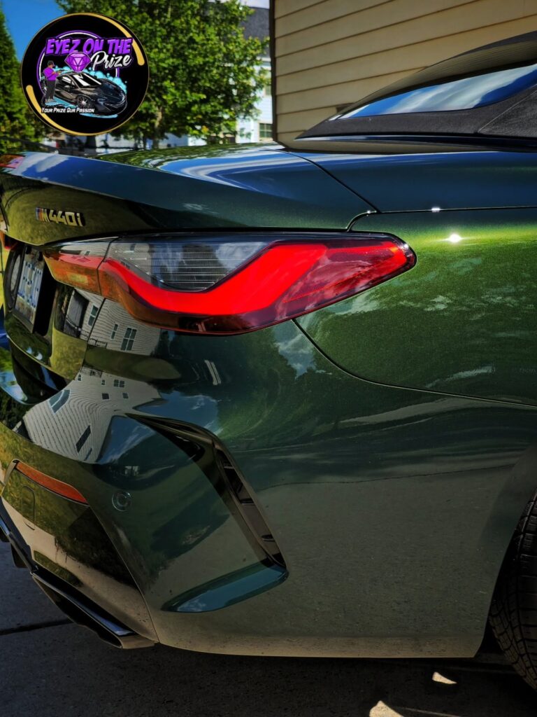 Close-up of a dark green BMW M440i convertible rear taillight and quarter panel with glossy reflective paint.