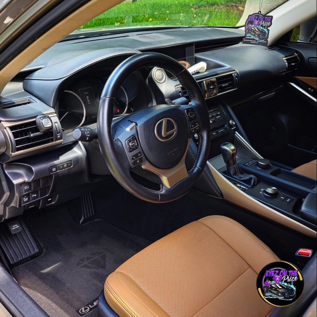 Driver side interior of a Lexus IS with clean tan leather seats, black steering wheel, and dashboard after detailing.