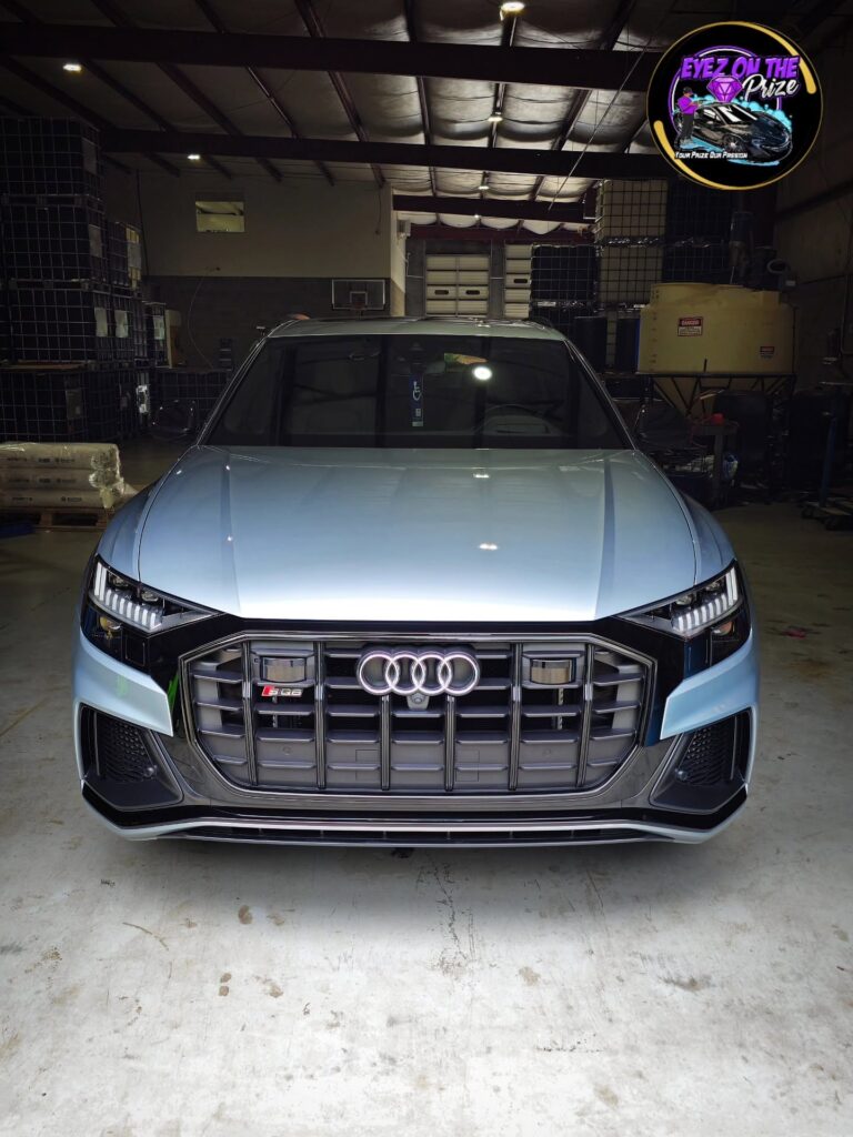 Light blue Audi SQ8 facing forward inside a warehouse shop, showing its black grille and clean glossy hood