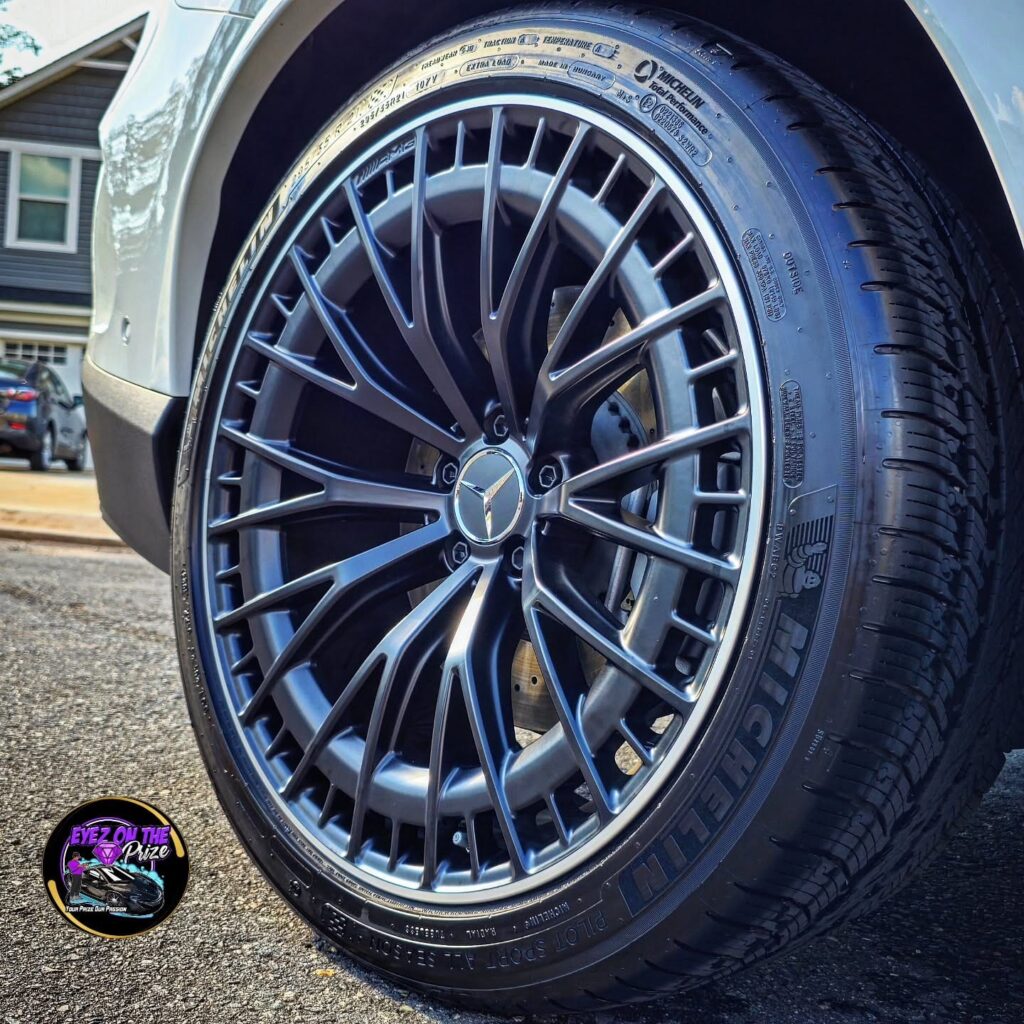 Close-up of a cleaned black multi-spoke Mercedes AMG wheel with Michelin Pilot Sport tire on a white SUV in a driveway.