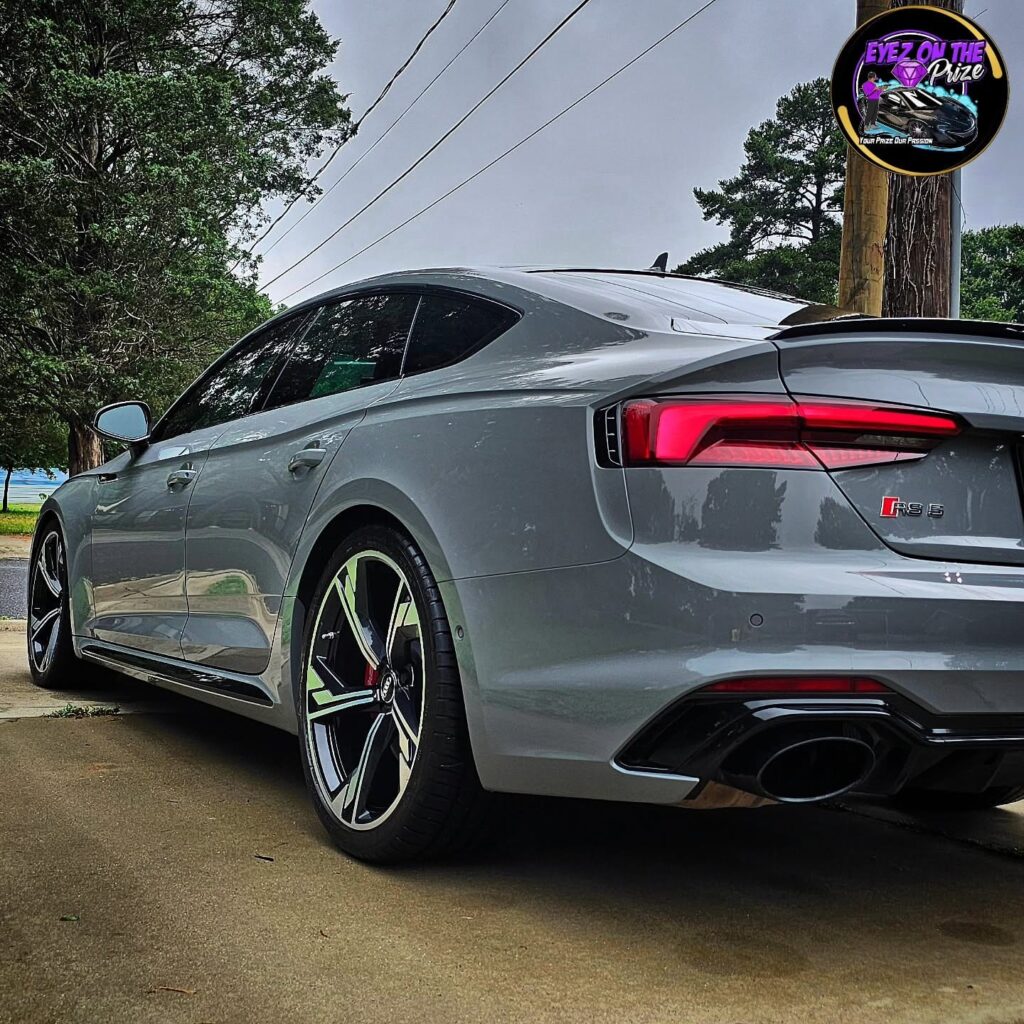 Rear quarter view of a nardo gray Audi RS5 Sportback with glossy paint and dark alloy wheels parked on a driveway.