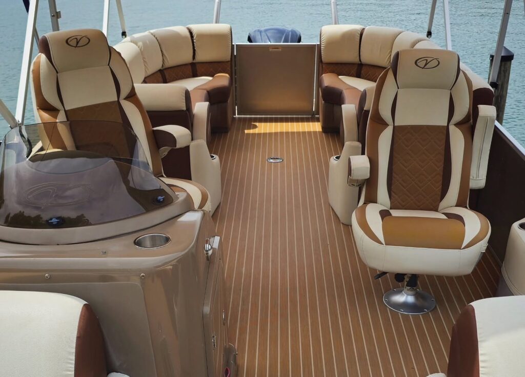 Pontoon boat interior with clean tan and cream upholstered seats and teak-style vinyl flooring at a dock