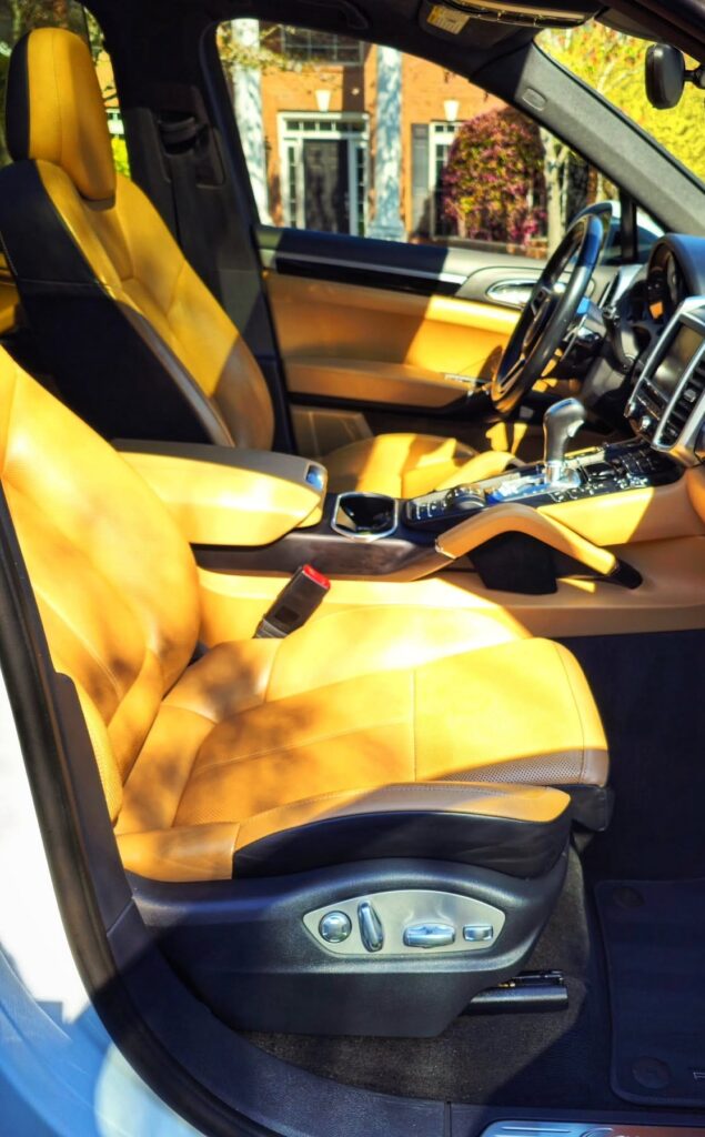 Porsche Cayenne front interior with cleaned tan leather seats, black carpet, and Porsche floor mat viewed through open