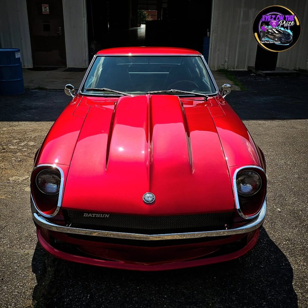 Front view of a red classic Datsun 240Z with glossy paint parked outside a garage building