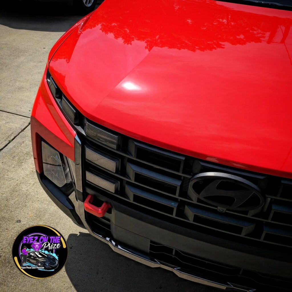 Close-up of a red Hyundai Santa Cruz front hood and black grille with glossy paint after detailing.