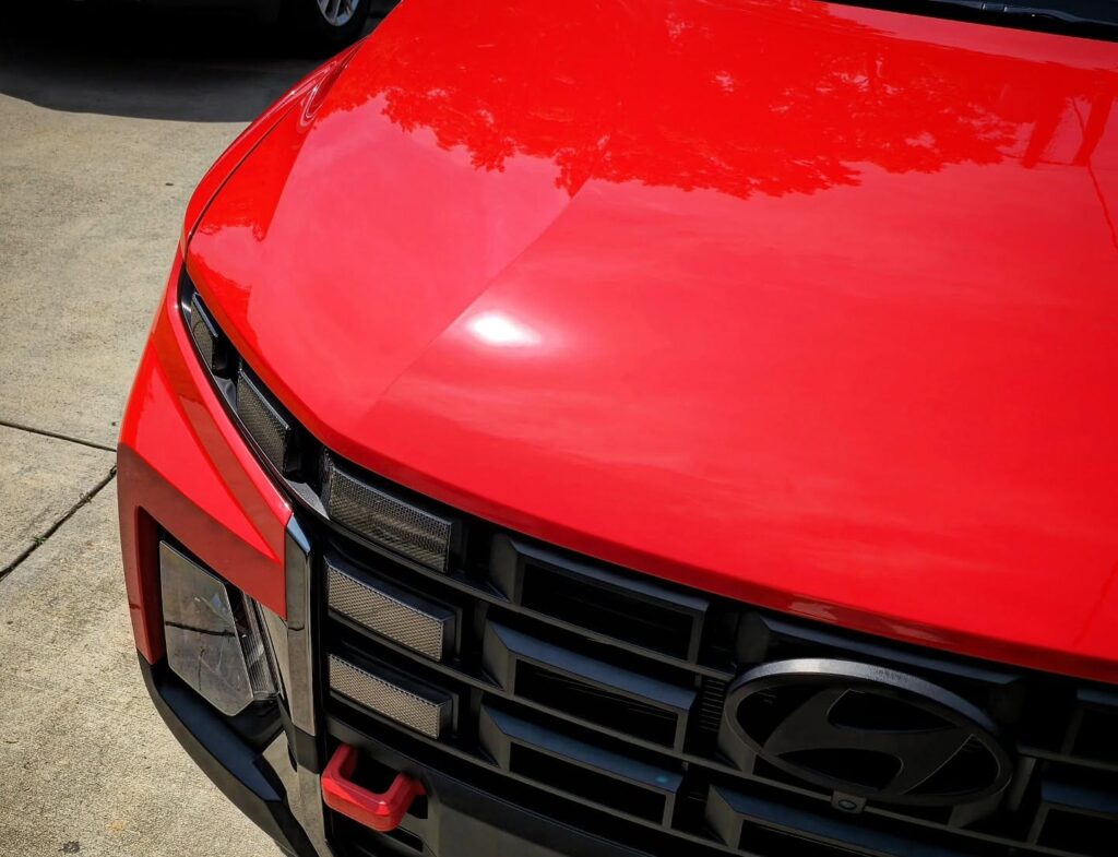 Close-up of a red Hyundai Santa Cruz front hood and black grille with glossy paint after detailing.