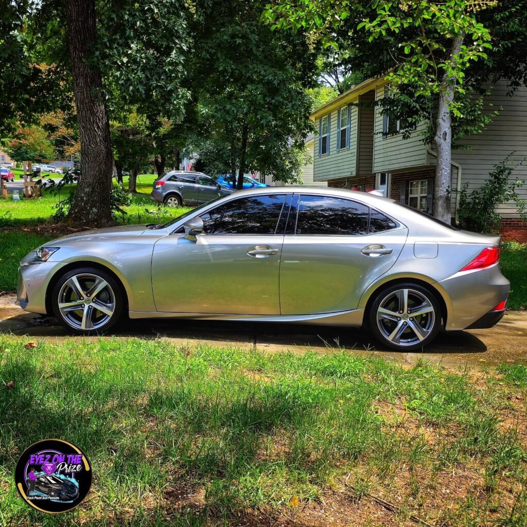 Side profile of a silver Lexus IS sedan with tinted windows parked in a residential driveway after detailing.