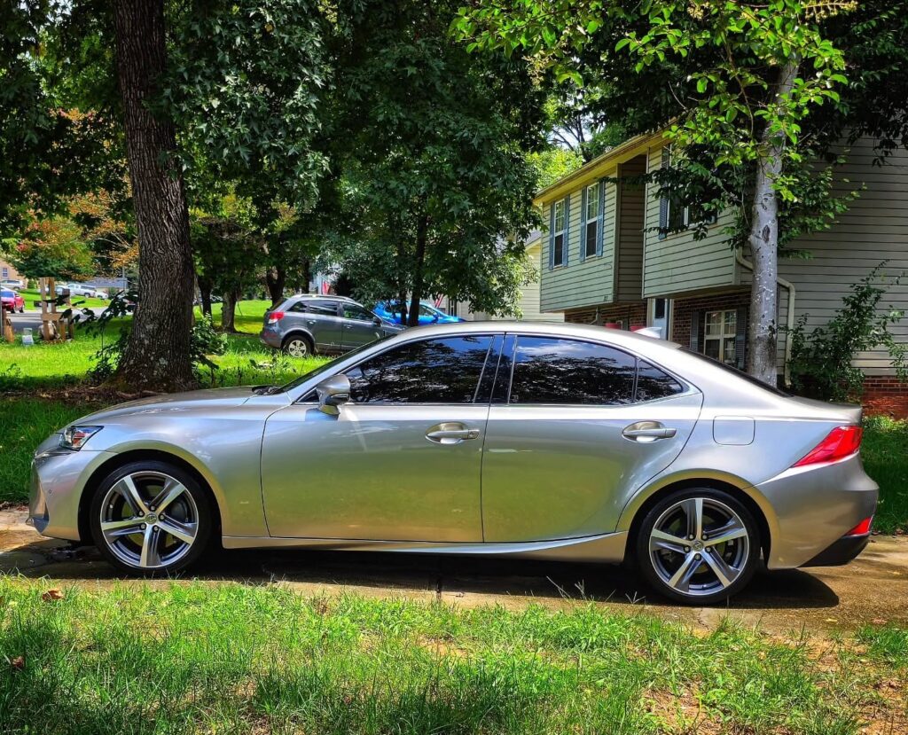 Side profile of a silver Lexus IS sedan with tinted windows parked in a residential driveway after detailing.
