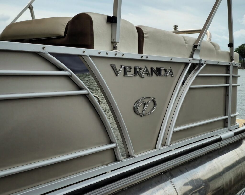 Side panel of a tan Veranda pontoon boat with clean fencing, rails, and upholstery, docked on a lake