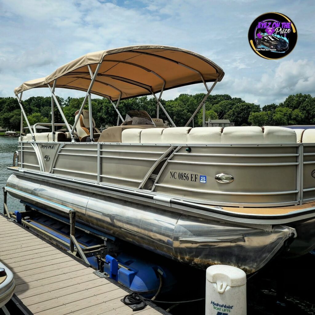 Tan Veranda pontoon boat with bimini top raised on a HydroHoist lift at a lake dock under a partly cloudy sky